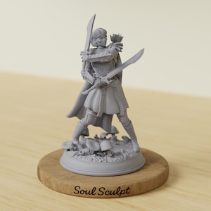 Può includere: Statuetta grigia di una donna guerriera che tiene due spade, in piedi su una base con funghi. La statuetta indossa un'armatura e un mantello. La base è su un supporto di legno con la scritta "Soul Sculpt".