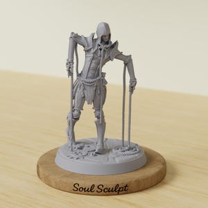 Può includere: Statuetta grigia di una persona in abiti medievali, che tiene delle corde, montata su una base di legno. La statuetta ha un cappuccio e abiti dettagliati. La base ha il testo "Soul Sculpt".