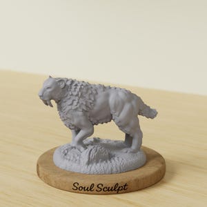 Puede incluir: Una escultura gris de un tigre dientes de sable, de pie sobre una pequeña base texturizada. La escultura está montada sobre una base de madera redonda. El texto "Soul Sculpt" está impreso en la base de madera.
