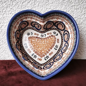 Könnte beinhalten: Herzförmige Keramikschale mit blauem Rand und aufwendigen Blumenmustern in Braun, Weiß und Marineblau. Das Innere der Schale weist ein detailliertes Design auf, ideal zum Servieren oder Ausstellen. Ein dekoratives Stück für Küche oder Esszimmer.