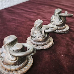 May include: Three dark bronze-toned metal drawer pulls, each featuring a sculpted animal head design with a circular ring handle attached to the mouth. The base of each pull is circular with a decorative beaded edge along the outer perimeter.