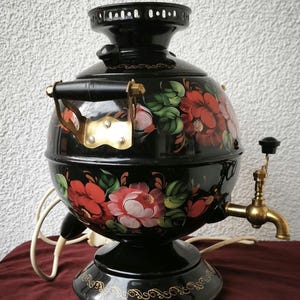 Peut inclure: Un samovar électrique noir avec un motif floral rouge, rose et vert. Le samovar a un robinet et une poignée en laiton, et une base noire. Le motif floral est peint à la main sur le corps arrondi.