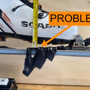 May include: A close-up of a white and black ski boot with a black metal ski binding. A yellow tape measure shows a measurement of approximately 7.6 cm. The word "PROBLEM" is in an orange speech bubble.