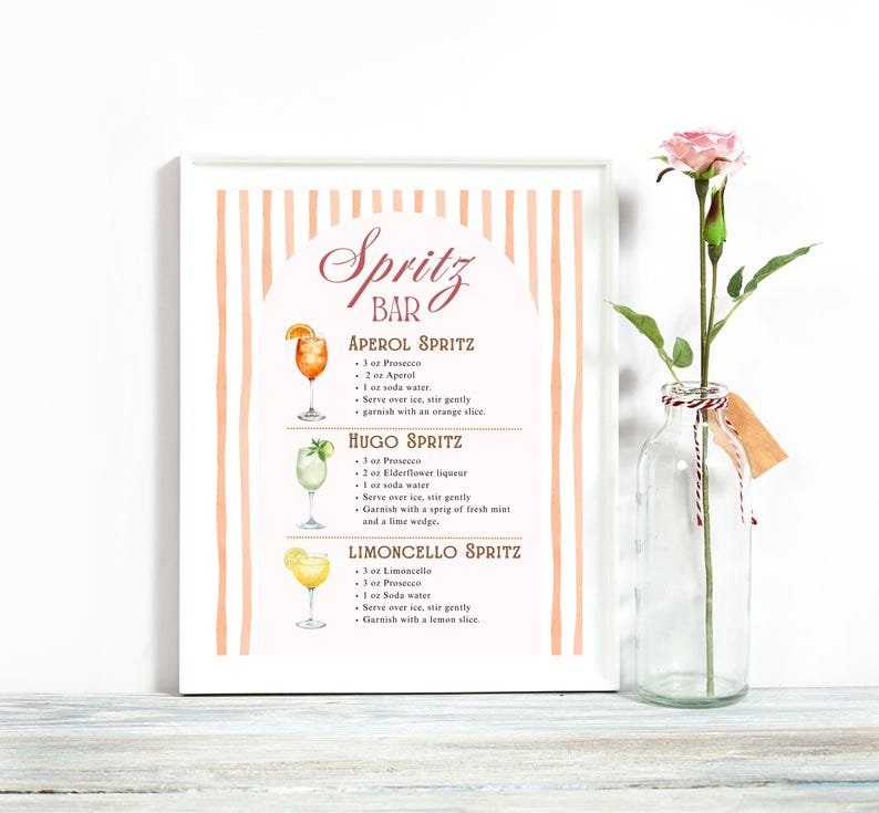 K&ouml;nnte beinhalten: Ein gerahmter Druck mit einem pfirsichfarbenen und wei&szlig;en gestreiften Hintergrund zeigt Cocktailrezepte, darunter Aperol, Hugo und Limoncello Spritz. Der Text "Spritz Bar" steht oben. Rechts ist eine klare Glasflasche mit einer rosa Rose.