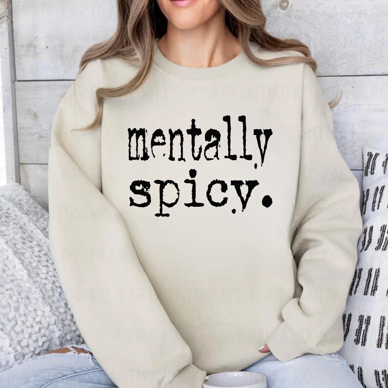 May include: A cream-colored sweatshirt with the words "mentally spicy" printed in black, bold letters. The sweatshirt has a crew neck and long sleeves. The text is centered on the front of the shirt.