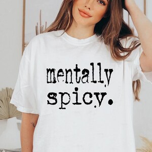 May include: White t-shirt with the phrase "mentally spicy" printed in black, bold letters. The shirt has a crew neck and short sleeves. The text is centered on the front of the shirt.