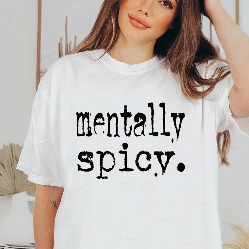 May include: White t-shirt with the phrase "mentally spicy" printed in black, bold letters. The shirt has a crew neck and short sleeves. The text is centered on the front of the shirt.