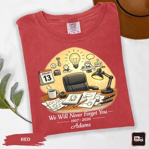 May include: Red t-shirt with a graphic design featuring a desk scene with a calendar, coffee cup, and a lightbulb. The text "We Will Never Forget You" and the name "Adams" are also printed on the shirt.