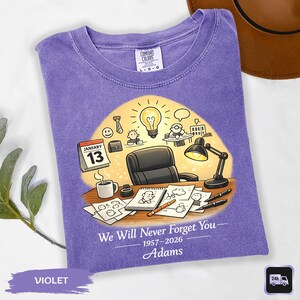 May include: Violet Comfort Colors t-shirt with a graphic of an office scene, including a desk, lamp, and calendar showing January 13. Text reads "We Will Never Forget You" and "Adams".