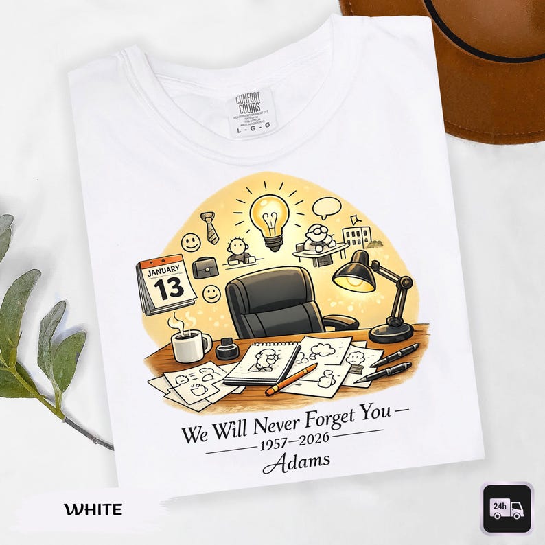 May include: White t-shirt with a colorful illustration of an office scene. The design includes a desk, lamp, calendar, and the text "We Will Never Forget You - 1957-2026 - Adams".
