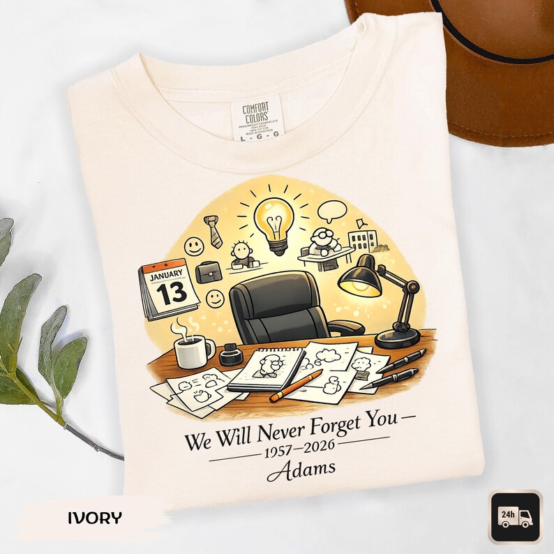 May include: Ivory-colored t-shirt featuring a desk scene with a calendar showing January 13th, a lightbulb, and the text "We Will Never Forget You - 1957-2026 - Adams." The shirt has a Comfort Colors label.