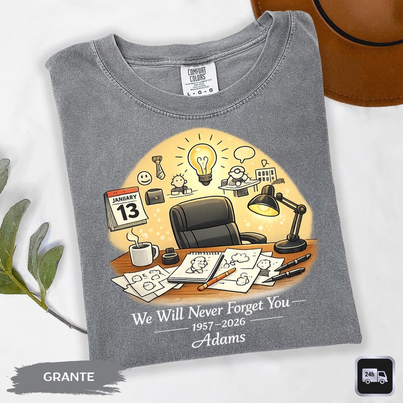May include: Gray t-shirt with a graphic of an office scene, including a desk, lamp, and calendar. The calendar shows January 13. Text on the shirt reads "We Will Never Forget You" and the name "Adams" with dates. The shirt has a Comfort Colors tag.