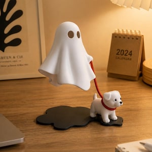 Peut inclure: Une figurine fantôme blanche avec des yeux bruns, reliée par une laisse rouge à une figurine de petit chien blanc avec un collier rouge. Les figurines sont sur une base noire en forme de nuage, pour une décoration amusante.