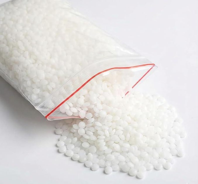 May include: A clear plastic bag with a red zipper is partially open, spilling out a pile of small, white, rounded beads. The beads are scattered on a white surface. The bag is filled with the same white beads.