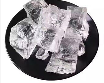 May include: A black plate holds several large, clear, irregularly shaped ice cubes. The ice cubes have a textured, almost crystalline appearance, reflecting light. The plate's dark color contrasts with the bright ice.