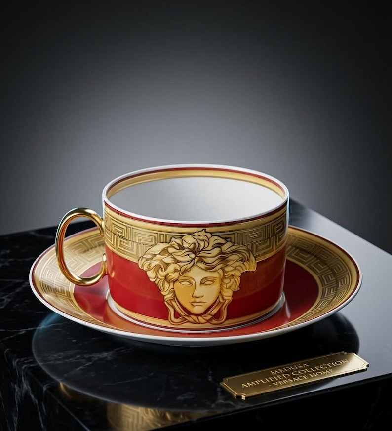 Puede incluir: Un juego de taza de t&eacute; y platillo de porcelana roja y dorada con un prominente emblema de cabeza de Medusa en oro. El borde est&aacute; decorado con un patr&oacute;n de greca dorada. Una peque&ntilde;a placa dorada dice MEDUSA AMPLIFIED COLLECTION - VERSACE HOME.