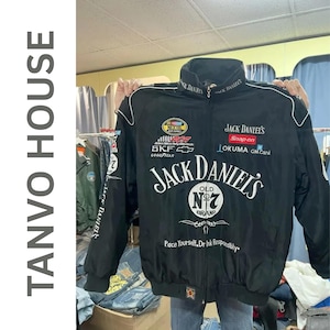 Puede incluir: Chaqueta de carreras negra con detalles blancos y varios logotipos de patrocinadores, incluyendo "Jack Daniel's". La chaqueta tiene cierre de cremallera y cuello alto. El texto "Pace Yourself, Dr Ink Responsibly" está impreso en la parte inferior.