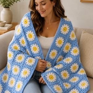 May include: A light blue crochet cardigan featuring a daisy pattern. The cardigan has a V-neck design and long sleeves. The daisies are white with yellow centers. The garment is made of soft yarn.