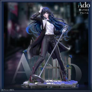 May include: A detailed figurine of a person with long blue hair, wearing a black suit and holding a microphone. The figure stands on a stage with a microphone stand and a fence. The background is blurred, with Japanese text in the upper right corner.