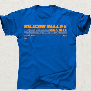 May include: A royal blue t-shirt with the words "SILICON VALLEY" in orange block letters above a circuit board design and the text "EST. 1971". The shirt is a crew neck style.