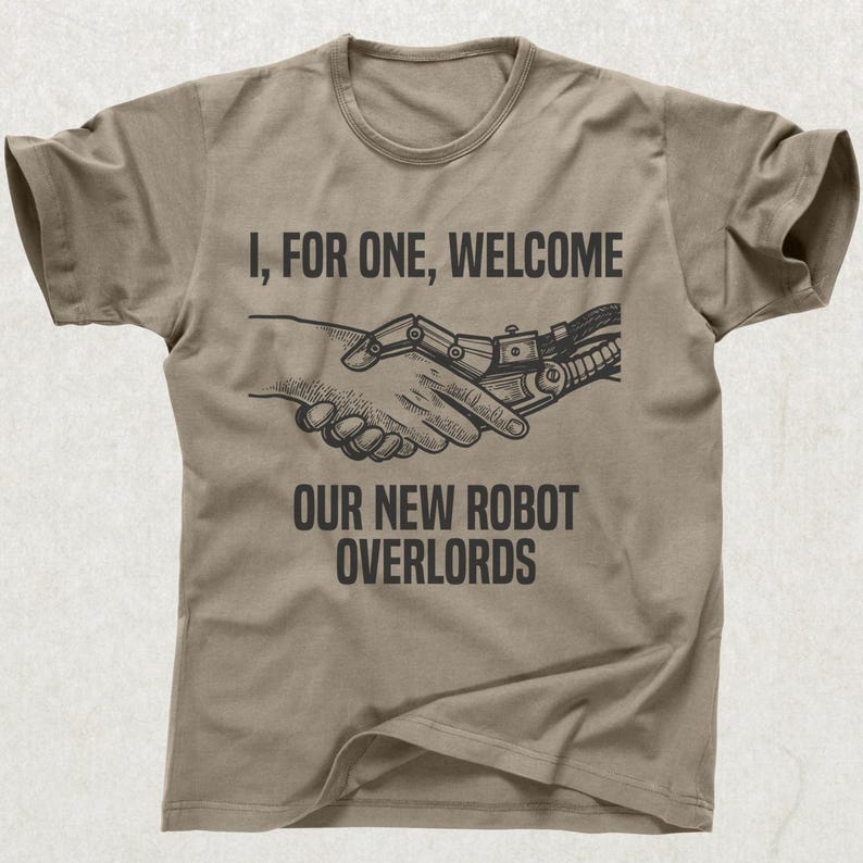 May include: Tan t-shirt with the text "I, FOR ONE, WELCOME OUR NEW ROBOT OVERLORDS" above an illustration of a human hand shaking a robotic hand. The design is in black.