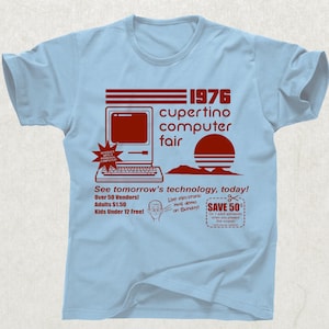 Peut inclure: T-shirt bleu clair avec un graphisme rouge annonçant la Cupertino Computer Fair de 1976. Le design comprend un ordinateur vintage, un soleil et le texte "See tomorrow's technology, today!" et "SAVE 50¢".