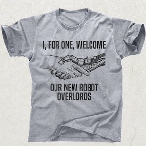May include: A gray t-shirt with a crew neck featuring the text "I, FOR ONE, WELCOME OUR NEW ROBOT OVERLORDS." The graphic shows a human hand shaking hands with a robotic hand.