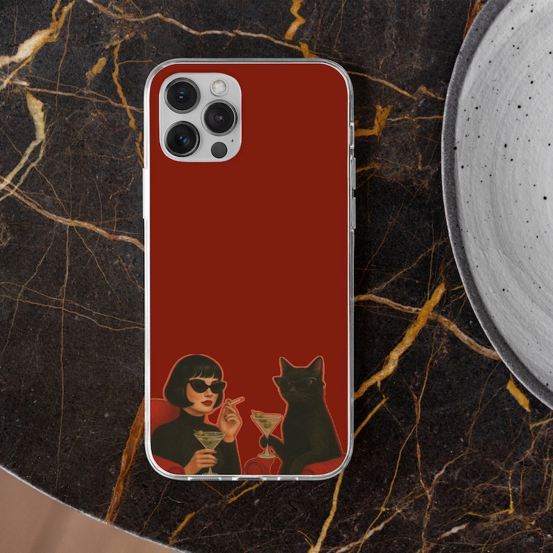 May include: A red phone case featuring an illustration of a woman and a black cat, both wearing sunglasses and holding martini glasses. The woman is smoking a cigarette. The case has a clear border and a camera cutout.