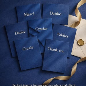Puede incluir: Un conjunto de tarjetas de agradecimiento azul marino con texto blanco en varios idiomas, incluyendo "Merci", "Danke", "Gracias", "Grazie" y "Thank you". Las tarjetas están dispuestas sobre una superficie azul texturizada con una cinta dorada y un sobre.