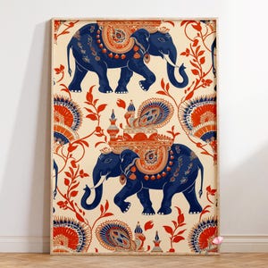 May include: Framed art print featuring two blue elephants with ornate orange and gold detailing. The elephants are set against a cream background with a repeating pattern of red floral elements and decorative fan-like shapes. The artwork is framed in a light wood.
