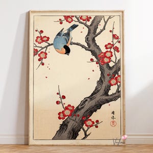 May include: A framed print featuring a bird perched on a tree branch with red blossoms. The bird has blue, orange, and black feathers. The tree trunk is dark gray, and the background is a light beige.