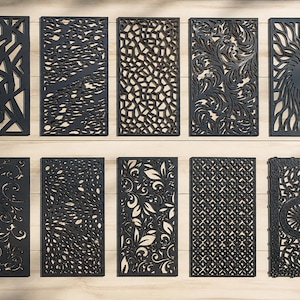 Può includere: Una collezione di dieci pannelli decorativi neri con intricati disegni ritagliati. I pannelli presentano vari modelli, tra cui forme geometriche, forme organiche e motivi floreali. I pannelli rettangolari sembrano essere in metallo o un materiale simile.