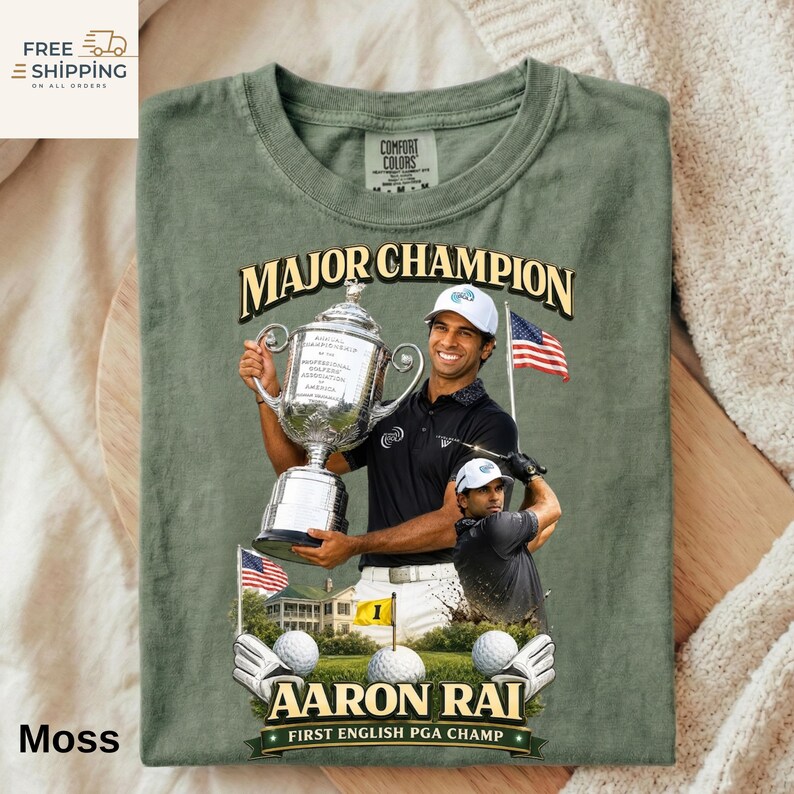 May include: Moss green t-shirt with a graphic of golfer Aaron Rai holding a trophy, text reads "MAJOR CHAMPION" and "FIRST ENGLISH PGA CHAMP". Includes golf balls, gloves, and an American flag.