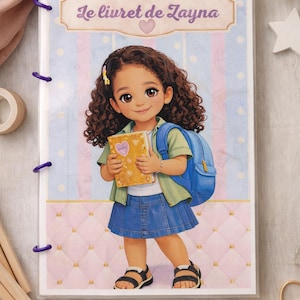 Può includere: Un quaderno con il testo "Le livret de Zayna" sulla copertina, con l'illustrazione di una ragazzina con i capelli ricci, uno zaino e un libro. Il quaderno ha anelli di rilegatura viola.