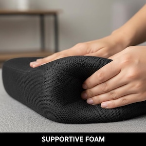 Op de afbeelding: Een zwart, ondersteunend schuimkussen wordt samengedrukt door twee handen. Het kussen heeft een mesh-achtige textuur. De tekst "SUPPORTIVE FOAM" wordt onderaan de afbeelding weergegeven.