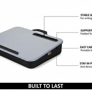 Op de afbeelding: Een grijze en zwarte laptoptafel met een handvat. De tafel heeft een gestructureerd oppervlak en een opstaande rand. De tekst op de afbeelding luidt "BUILT TO LAST", "STABLE & STURDY", "SUPPORTIVE FOAM", "EASY CARRY HANDLE" en "STAY-IN-PLACE LEDGE".