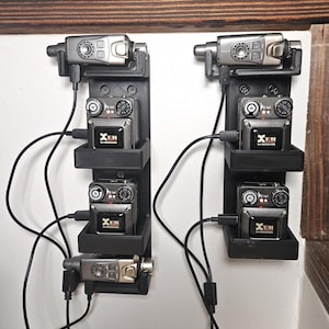 May include: Two black 3D-printed wall mounts holding six Xvive U4 wireless audio devices. Each mount features three slots with connected black USB charging cables. The devices are grey and black with visible dials, buttons, and the Xvive logo.