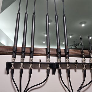 Pu&ograve; includere: Un set di otto antenne nere montate su due staffe metalliche nere. Sei antenne sono lunghe e due sono corte, ognuna dotata di connettori BNC argentati alla base. Cavi coassiali neri sono collegati ai connettori e si estendono verso il basso.