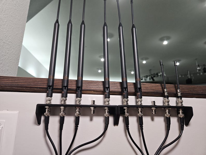Pu&ograve; includere: Un set di otto antenne nere montate su due staffe metalliche nere. Sei antenne sono lunghe e due sono corte, ognuna dotata di connettori BNC argentati alla base. Cavi coassiali neri sono collegati ai connettori e si estendono verso il basso.