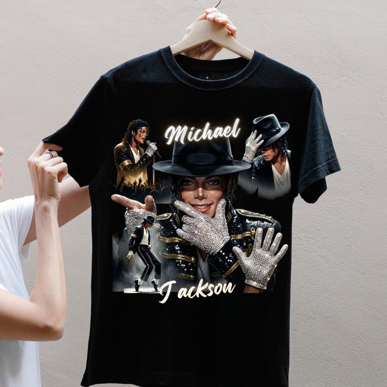 May include: Black t-shirt featuring multiple images of Michael Jackson, including a portrait with a black hat and jeweled gloves. The name "Michael Jackson" is written in white script across the shirt.