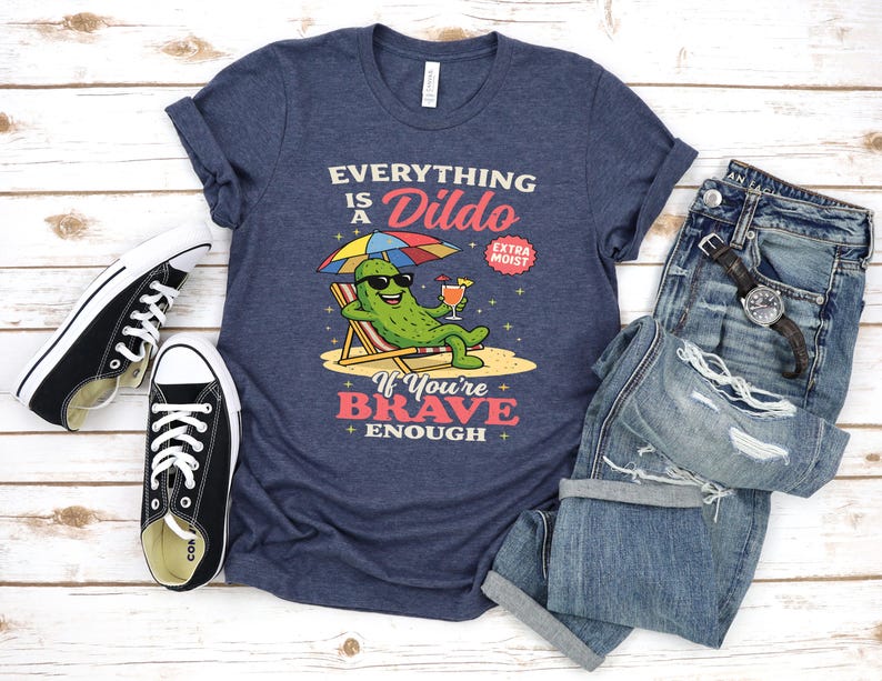 May include: Navy blue t-shirt with the text "Everything is a Dildo" and a cartoon pickle character relaxing on a beach chair. The shirt is paired with blue jeans and black sneakers.