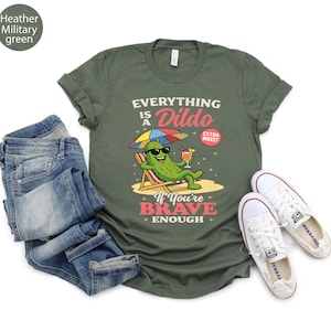 May include: Heather military green t-shirt with the text "EVERYTHING IS A DILDO" and a cartoon pickle wearing sunglasses, relaxing on a beach chair, holding a cocktail. The shirt is paired with blue jeans and white sneakers.