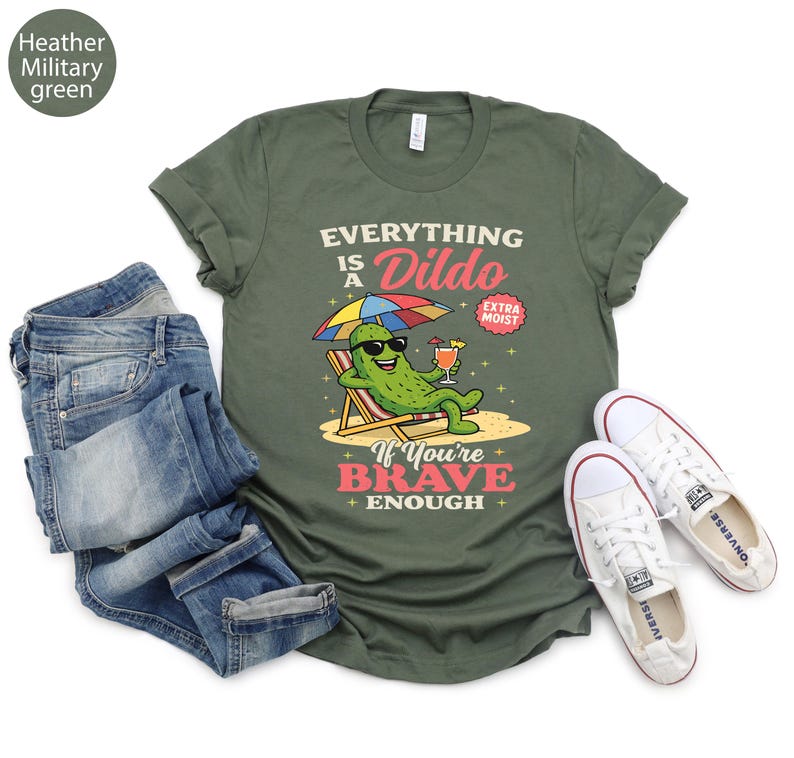 May include: Heather military green t-shirt with the text "EVERYTHING IS A DILDO" and a cartoon pickle wearing sunglasses, relaxing on a beach chair, holding a cocktail. The shirt is paired with blue jeans and white sneakers.