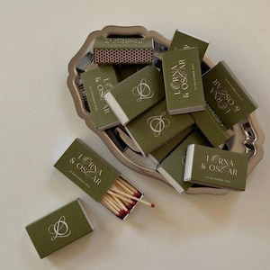 May include: A white ceramic mug with a black handle and the text "But First, Coffee" in a black, handwritten-style font. The mug is on a white surface.