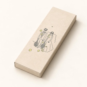 May include: A rectangular beige cardboard box featuring a black line art illustration of two figures in formal attire holding tennis rackets, surrounded by several small yellow tennis ball icons printed on the top surface.
