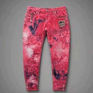 May include: Red and black tie-dye jeans featuring a cat face patch on the right hip, silver-tone metal rivets, a small hanging charm on the front pocket, and vertical silver-tone zippers at the bottom of each leg hem with a button closure.