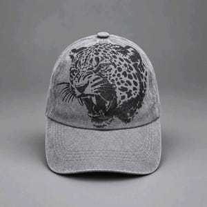 May include: A grey baseball cap with a distressed, washed-out finish. The front panel features a large, black graphic print of a snarling leopard head with visible spots and whiskers. The cap has a curved brim with visible stitching detail.