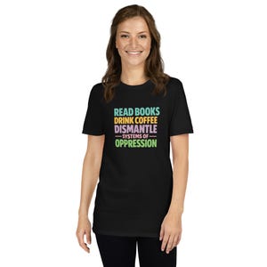 Puede incluir: Camiseta negra con el texto "READ BOOKS DRINK COFFEE DISMANTLE SYSTEMS OF OPPRESSION" en turquesa, amarillo, morado y verde. La camiseta es de cuello redondo y tiene mangas cortas.