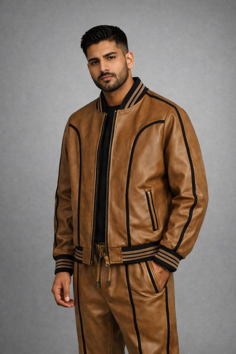 Pu&ograve; includere: Giacca bomber e pantaloni coordinati in pelle marrone con strisce e finiture nere. La giacca ha una chiusura con zip e polsini e orlo a coste. I pantaloni hanno una vita con coulisse e tasche.