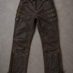 Puede incluir: Pantalones de color marrón oscuro con cierre frontal de cordones, dos correas con hebilla ajustables en cada muslo y detalles de cordones verticales a lo largo de la parte inferior de las piernas. Incluyen anillas en D de metal en la cintura.
